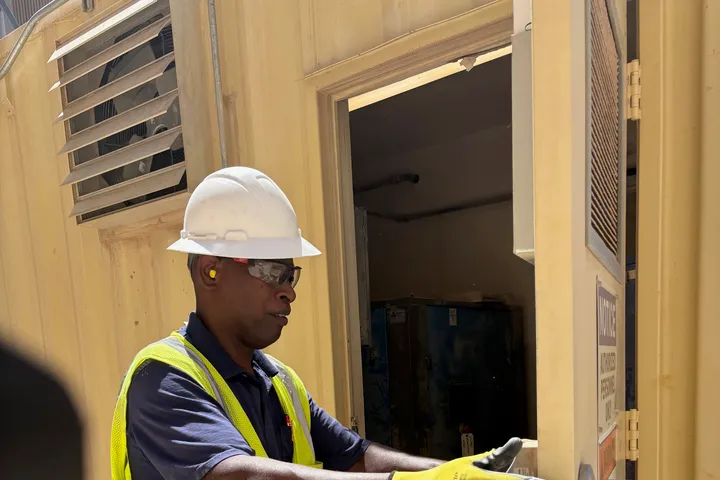 Pleasant Air technician in a hard hat and safety vest opening an outdoor equipment enclosure