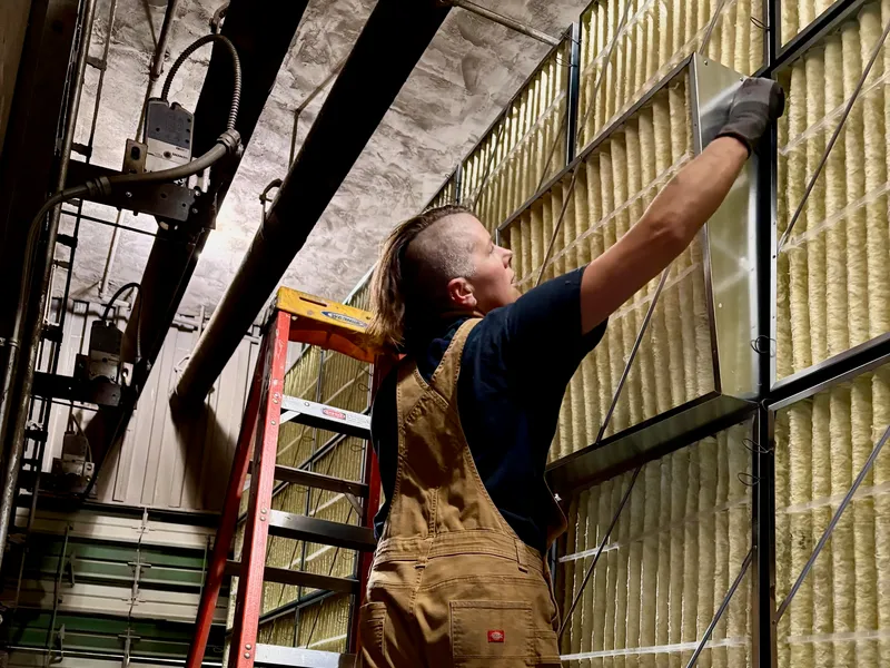 Pleasant Air technician on a ladder swapping filters in a floor-to-ceiling filter bank