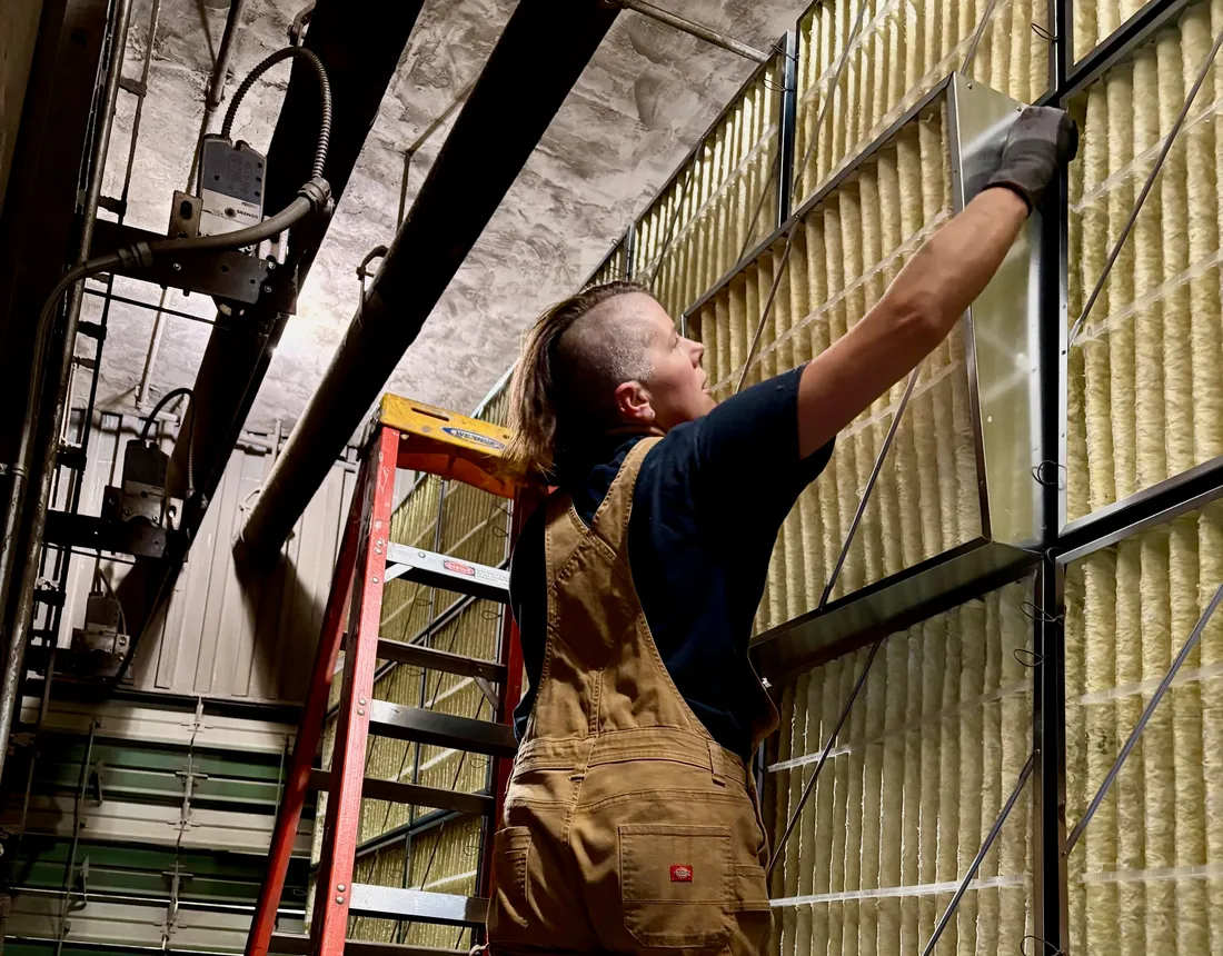 Pleasant Air technician on a ladder swapping filters in a floor-to-ceiling filter bank