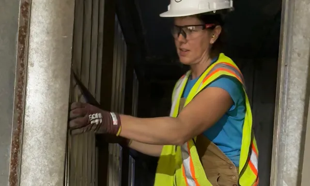 Pleasant Air technician in a hard hat and safety vest kneeling inside an air handler to fit a filter