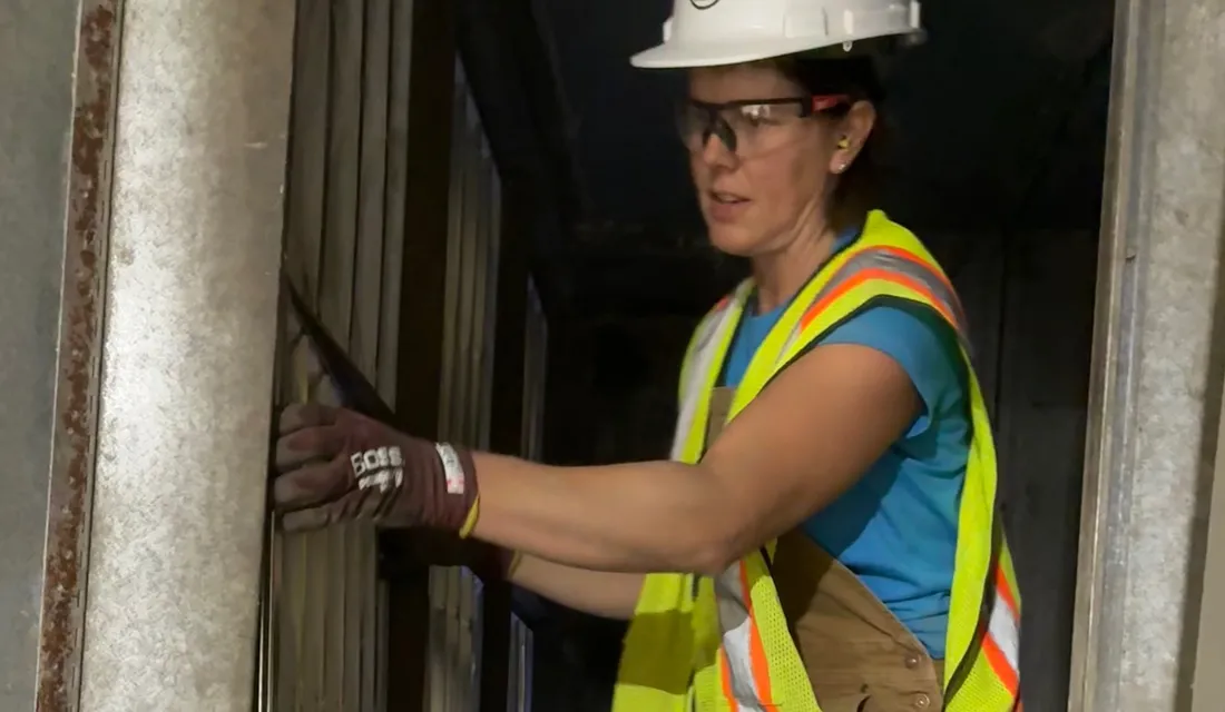 Pleasant Air technician in a hard hat and safety vest kneeling inside an air handler to fit a filter